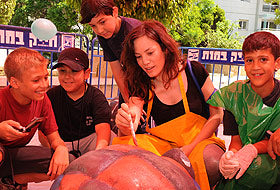 ריקי בליך עומדת לצד פסל "צב השעה" - יצירת אמנות ירוקה עשויה מחומרים ממוחזרים מבית וינקלר אנדרטאות